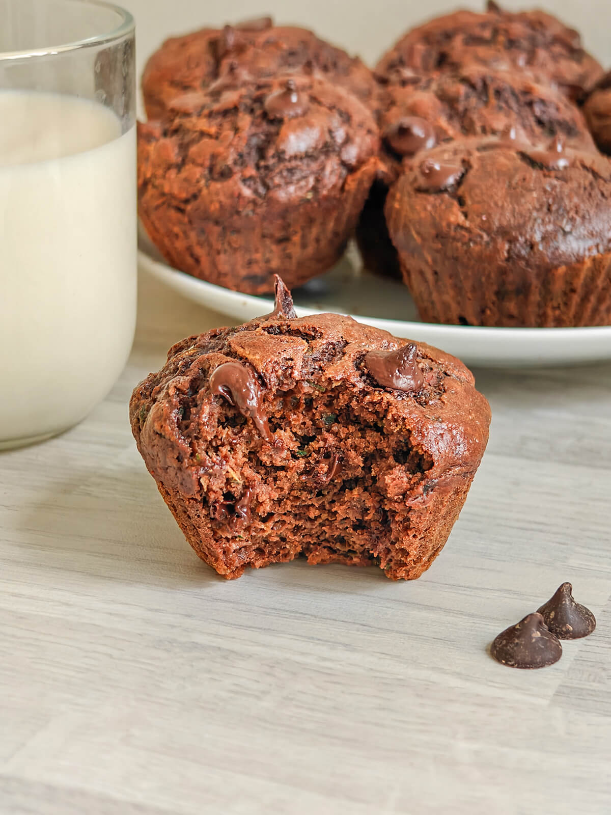 Un muffin chocolat et courgette, verre de lait et muffins chocolat en fond.
