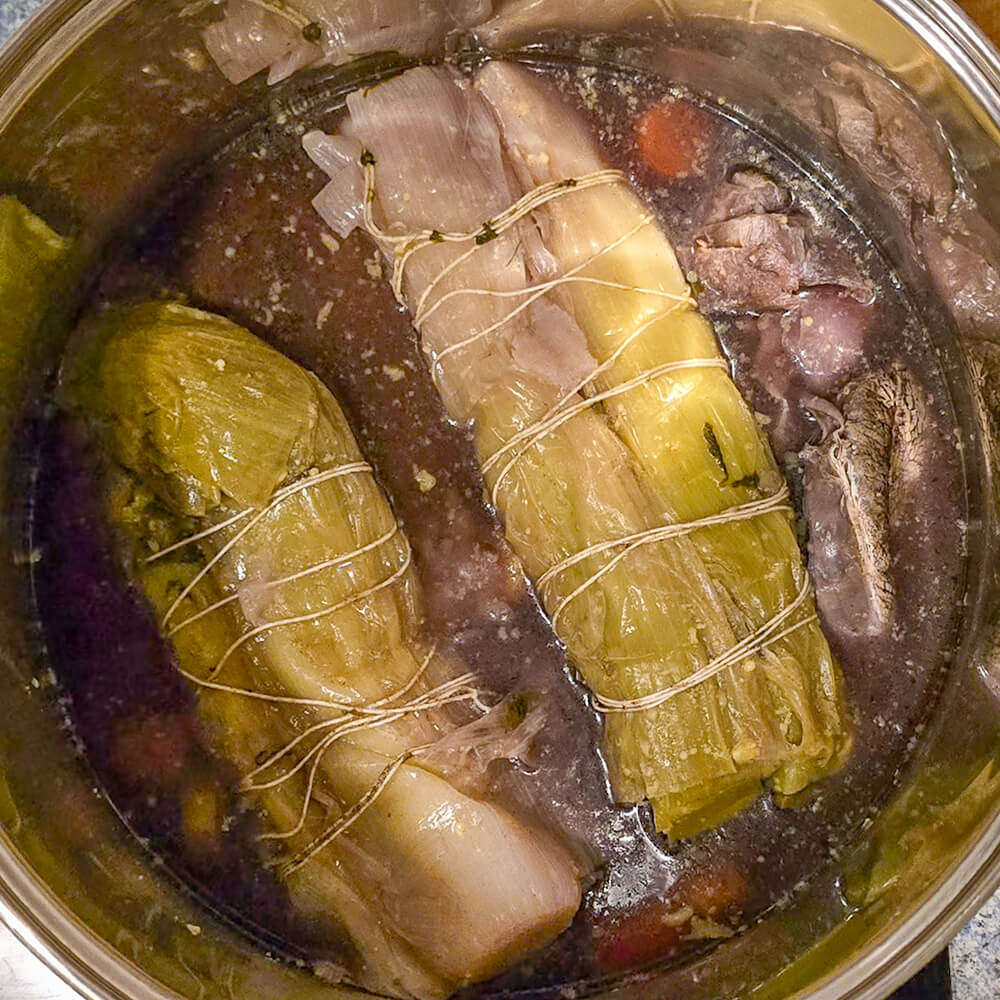 Deux gros bouquets de poireaux ficelés avec de la ficelle de cuisine cuisant dans la marmite de pot-au-feu.