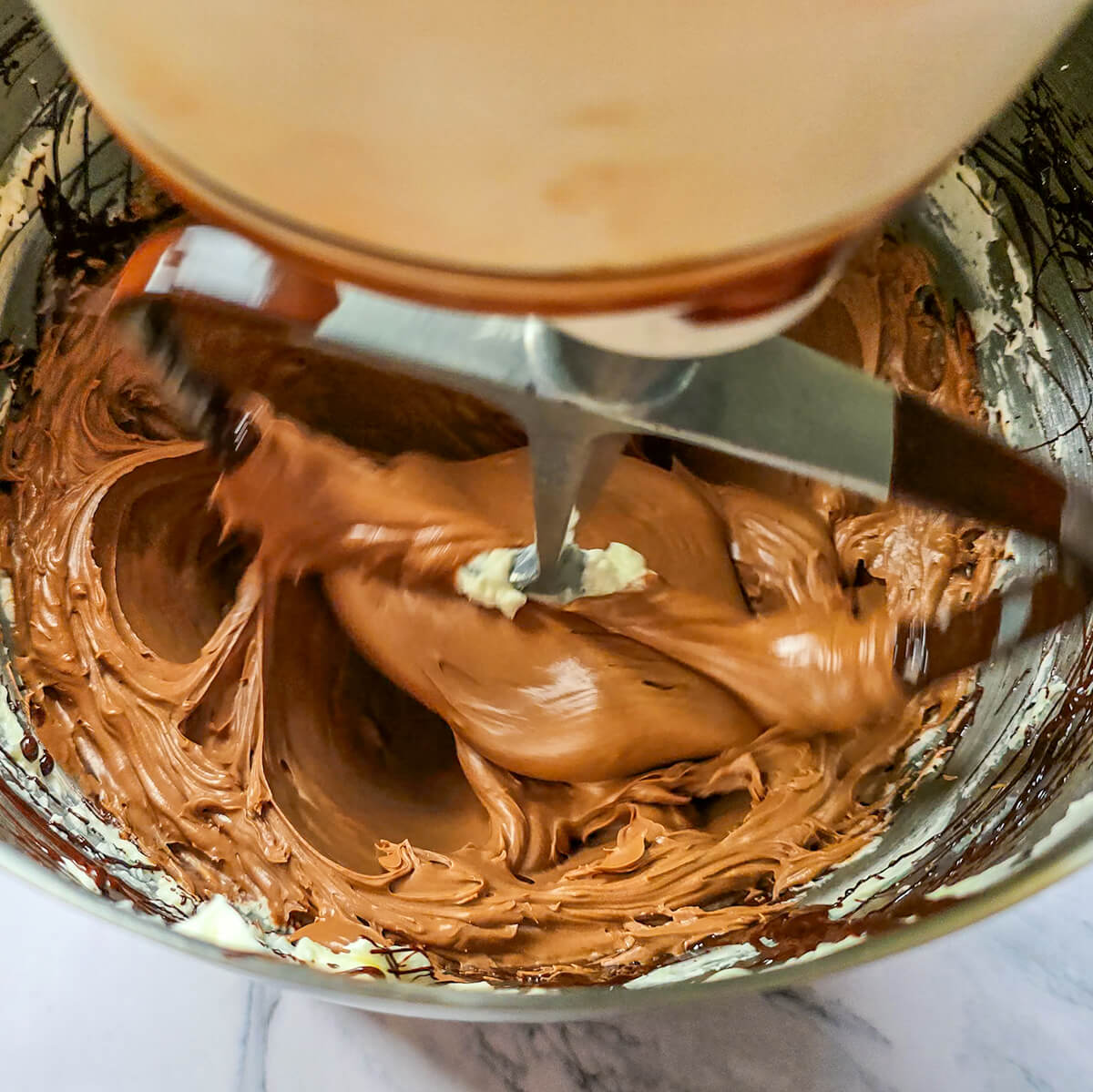 Robot pâtissier en train de mélanger une crème au beurre au chocolat noir lisse et brillante pour garnir des cupcakes vanille moelleux.