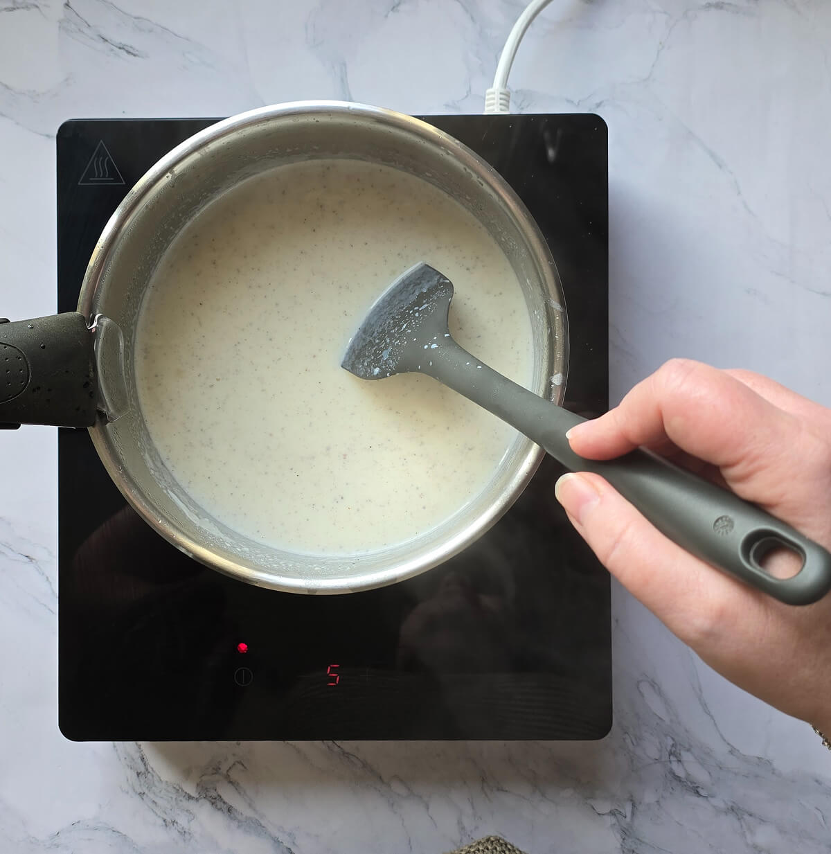 Une main mélangeant une sauce béchamel dans une casserole.