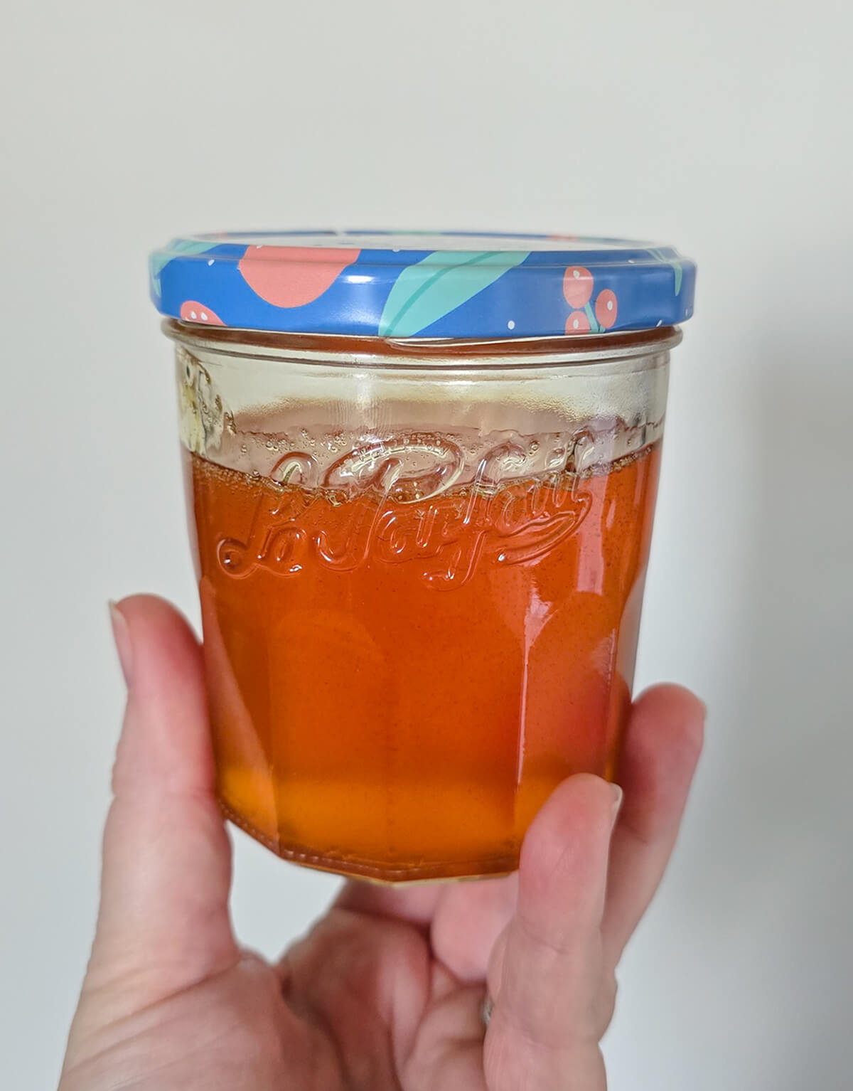 Une main tenant un pot de confiture rempli de caramel liquide maison.
