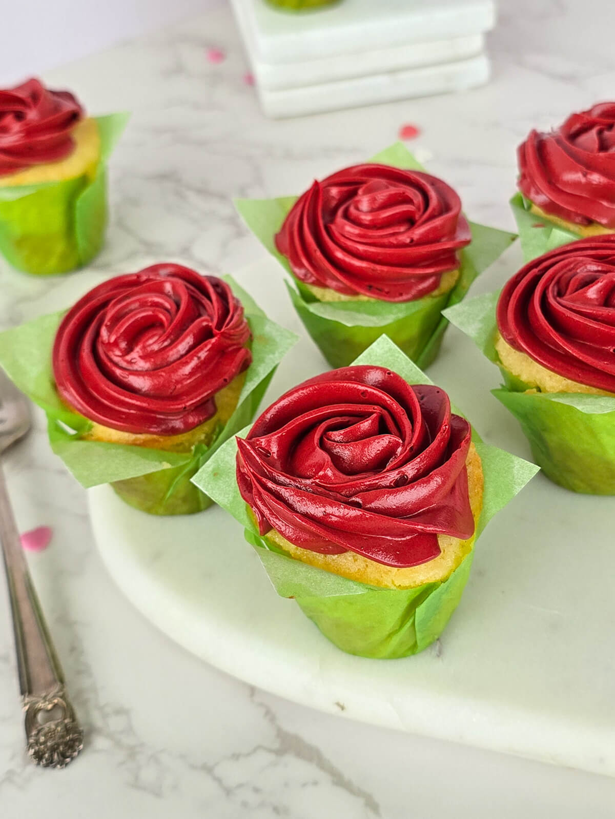 Des cupcakes vanille avec une crème au beurre rouge vif, présentés sur une planche marbrée blanche.