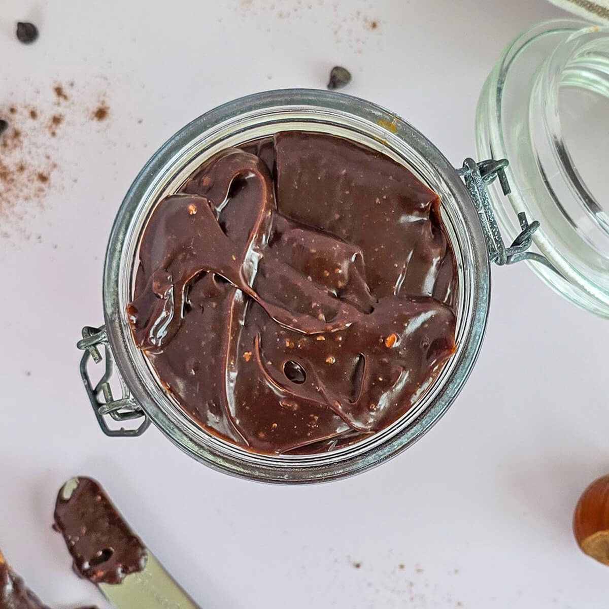 Gros plan sur un bocal en verre rempli de pâte à tartiner maison onctueuse au chocolat noir et éclats de noisettes, texture brillante et lisse.