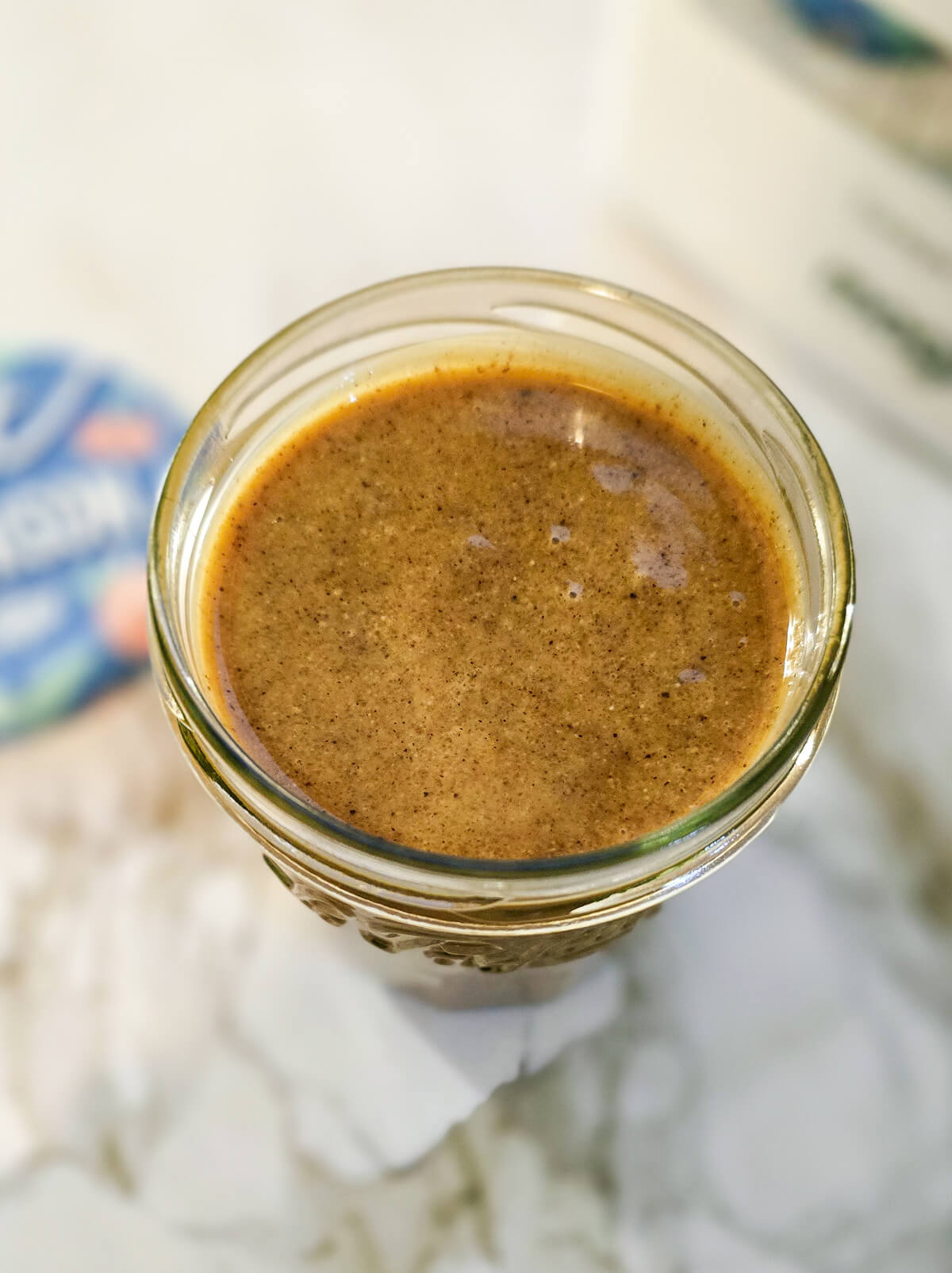 Du praliné noisette fait maison dans un pot de confiture, sur un plan de travail blanc marbré.