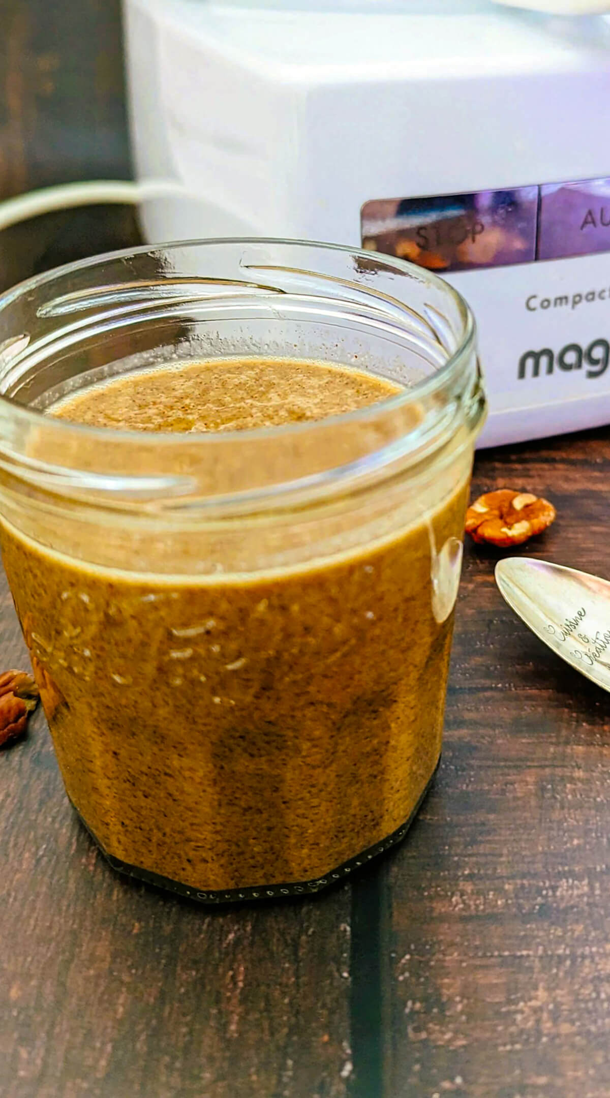 Du praliné pécan fait maison dans un pot de confiture, robot mixeur Magimix en arrière plan.