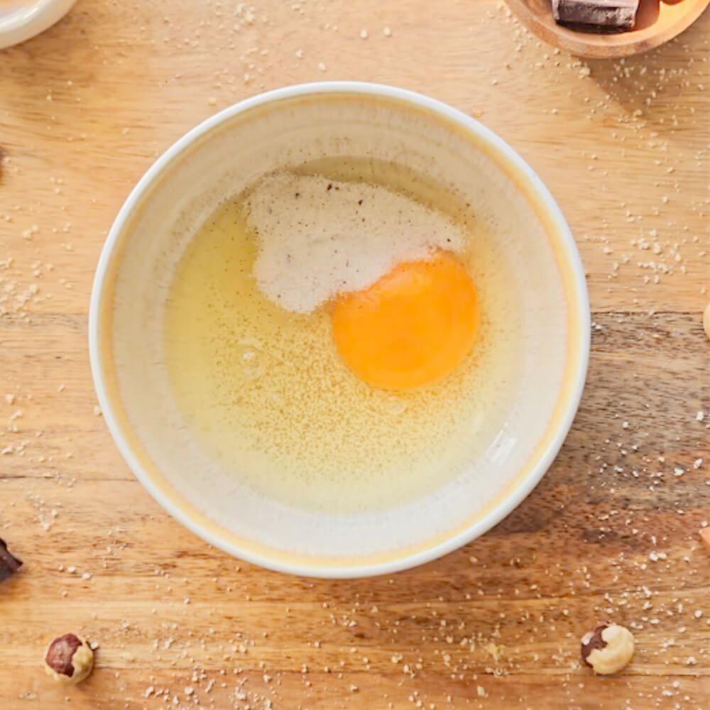 Vue de dessus d'un bol contenant un œuf entier et du sucre de canne, les premiers ingrédients d'un bowlcake praliné chocolat noir.
