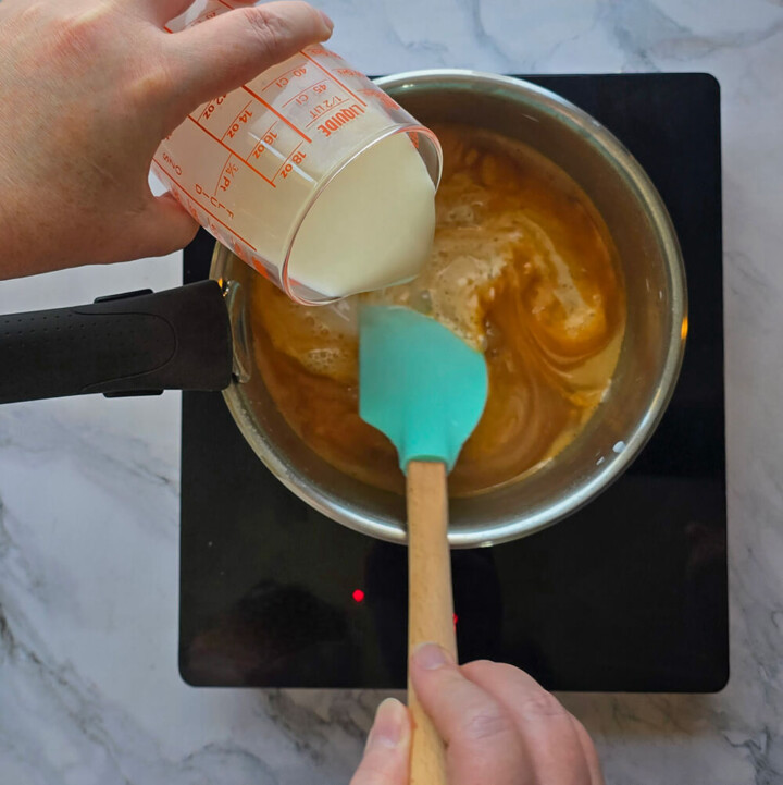 Une main versant du lait dans une casserole pour réaliser une crème dessert.