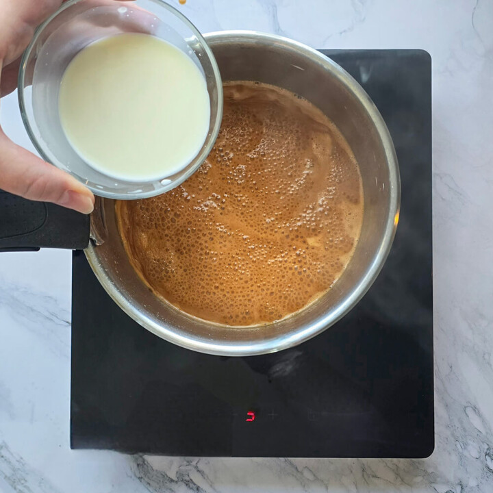 Une main ajoutant de la maizena dans une casserole pour faire une crème dessert caramel.