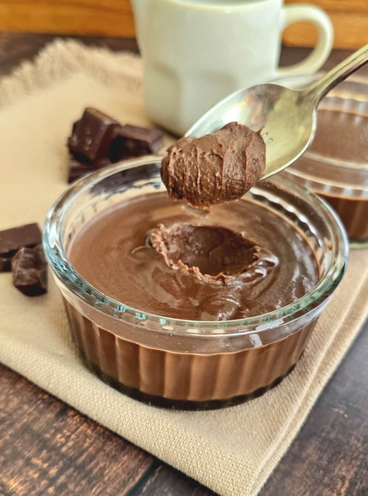 Deux ramequins en verre garnis de crème chocolat lait concentré onctueuse, présentés avec des carrés de chocolat noir sur une serviette en lin clair.