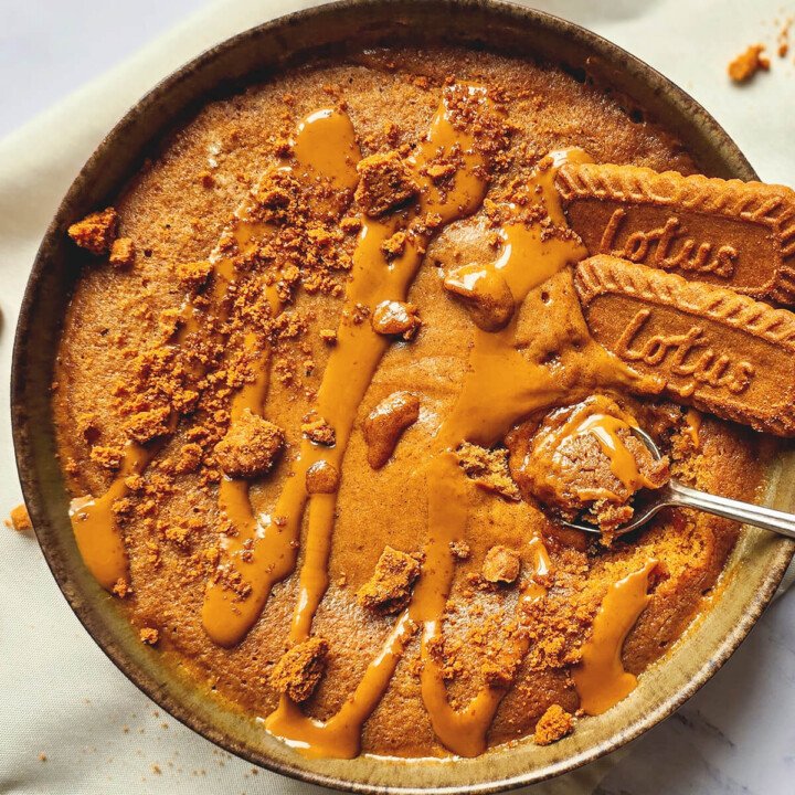 Gros plan sur une cuillère remplie de bowlcake moelleux au spéculoos, brillant de nappage fondant. En arrière-plan, le bol et des biscuits Lotus entiers.