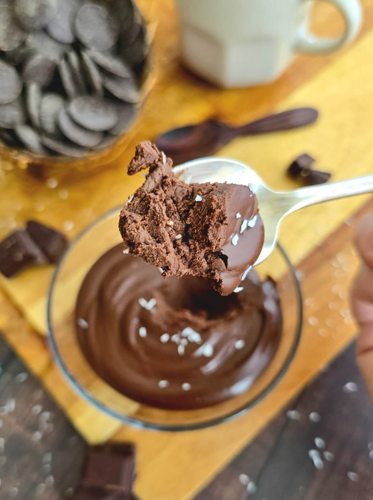 Gros plan sur une cuillère prélevant une dose de crème dessert onctueuse au chocolat et crème de coco, révélant une texture dense et fondante parsemée de copeaux de noix de coco.