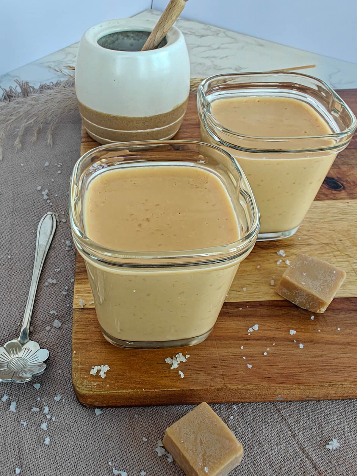Deux crèmes dessert au caramel avec une pointe de sel; sur une planche de bois, avec des fudges au caramel.
