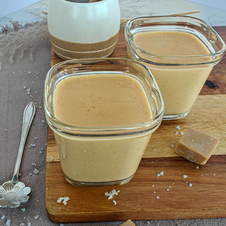 Deux crèmes dessert au caramel avec une pointe de sel; sur une planche de bois, avec des fudges au caramel.