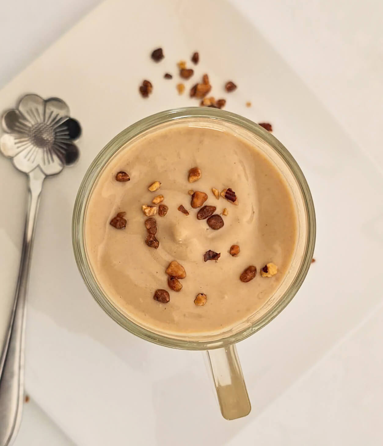 Une ctème dessert maison dans une verrine en verre, cuillère sur le coté, et pralin croustillant sur la crème.