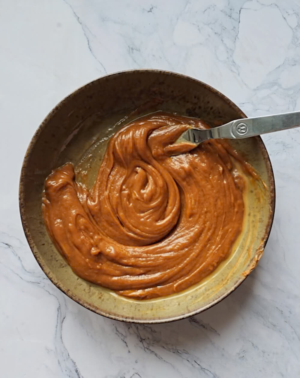 Mélange homogène de pâte à tartiner spéculoos et d'œuf dans un bol brun pour la base du bowlcake.