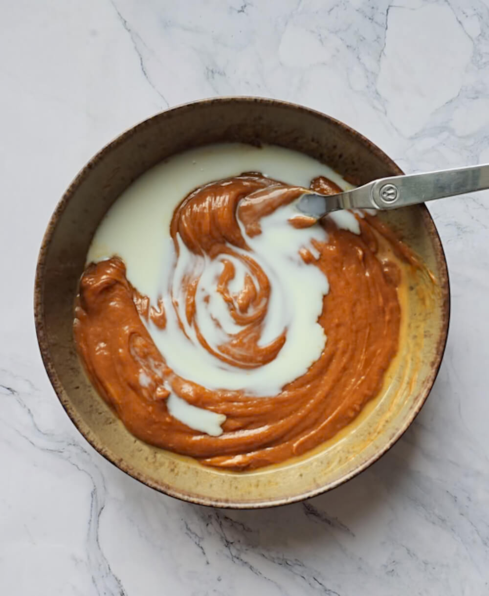 Ajout d'un filet de lait sur la base au spéculoos, créant un tourbillon blanc dans la préparation onctueuse.