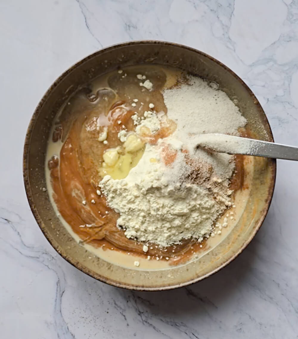 Ajout des ingrédients secs (farine, levure) sur le mélange liquide dans le bol avant l'étape finale du mélange.