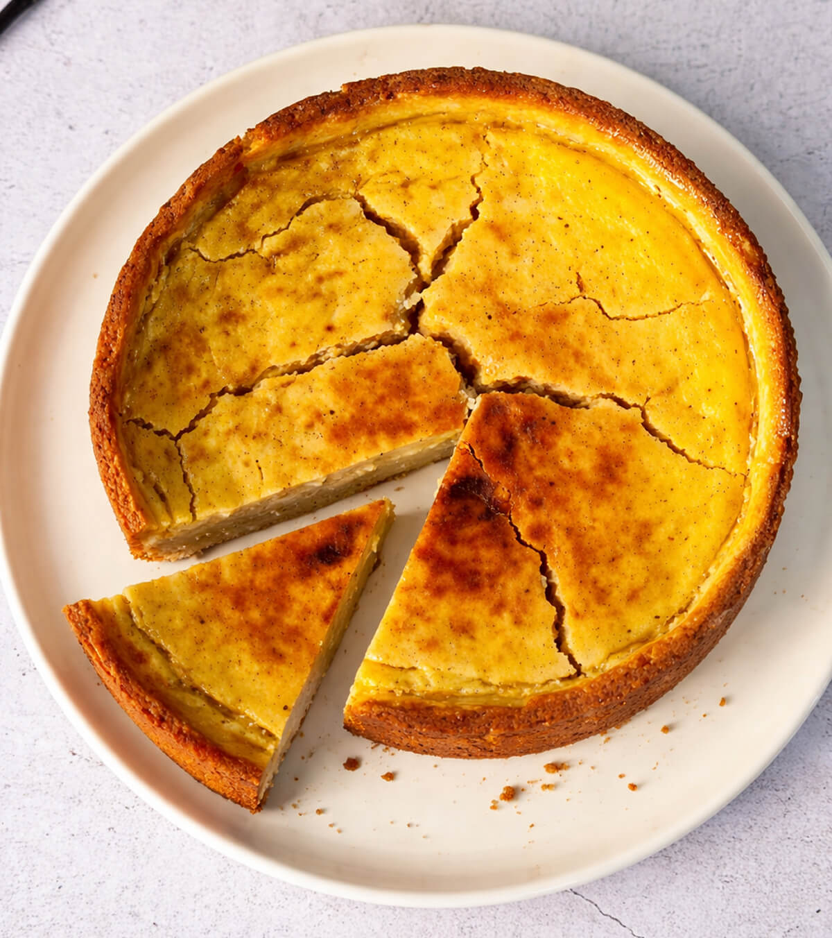 Un flan patissier qui présente des fissures sur le dessus, sur une assiette blanche.