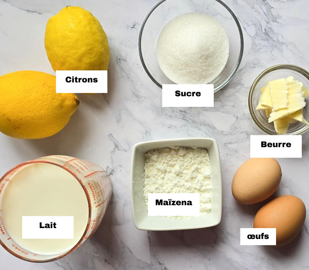 Des ingrédients pour réaliser des crèmes dessert au citron jaune, sur un fond blanc marbré.