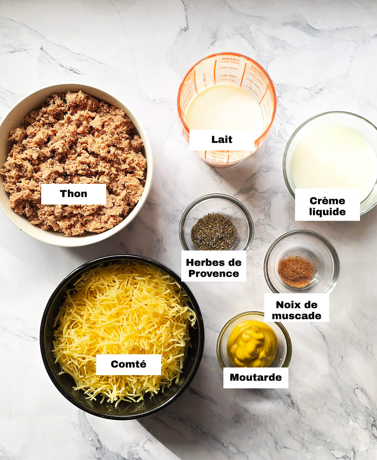 Des ingrédients pour réaliser un gratin de pâtes au thon, sur un fond marbré blanc.