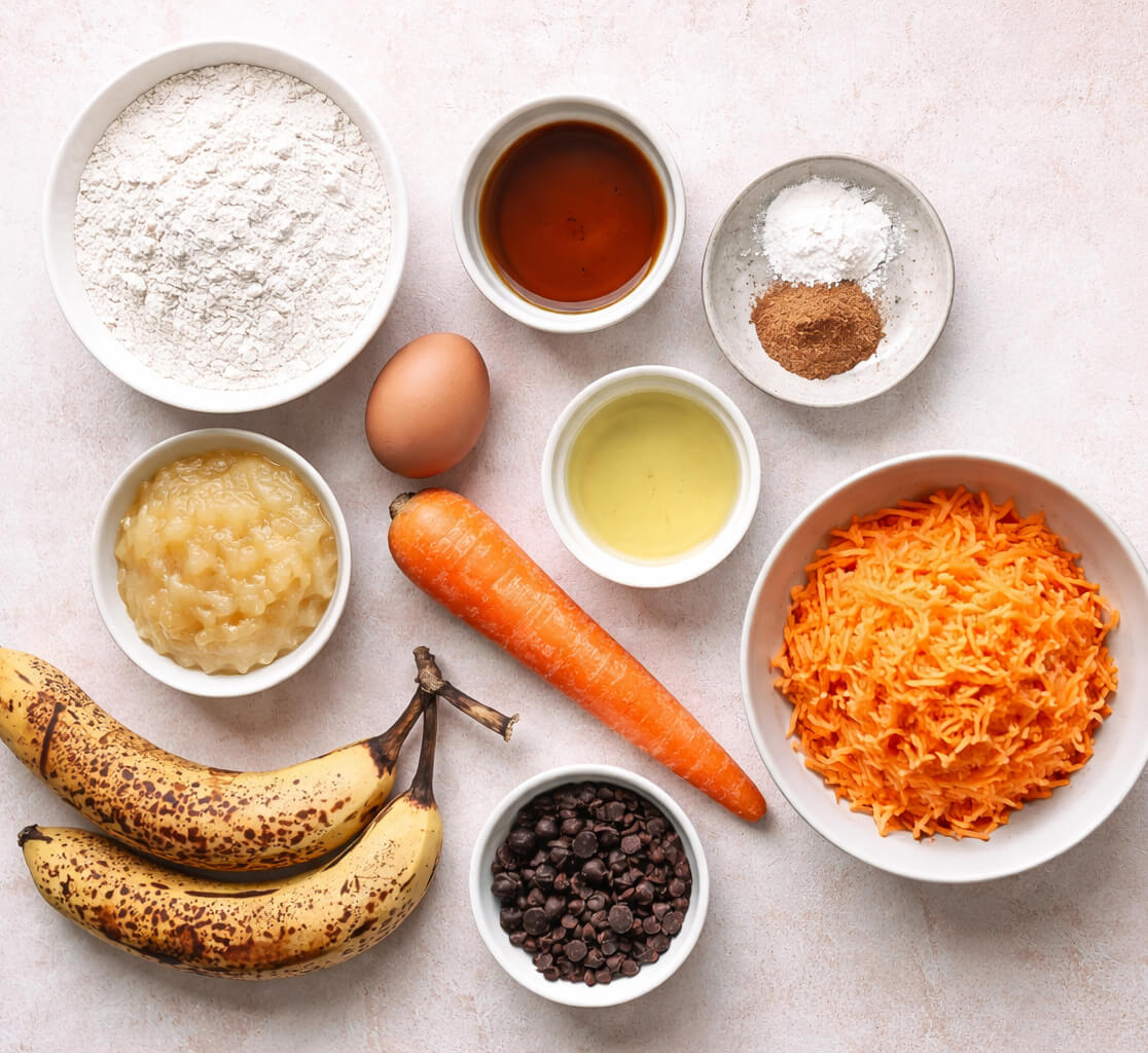 Des ingrédients pour faire des muffins pommes banane carotte sur un fond rose clair.