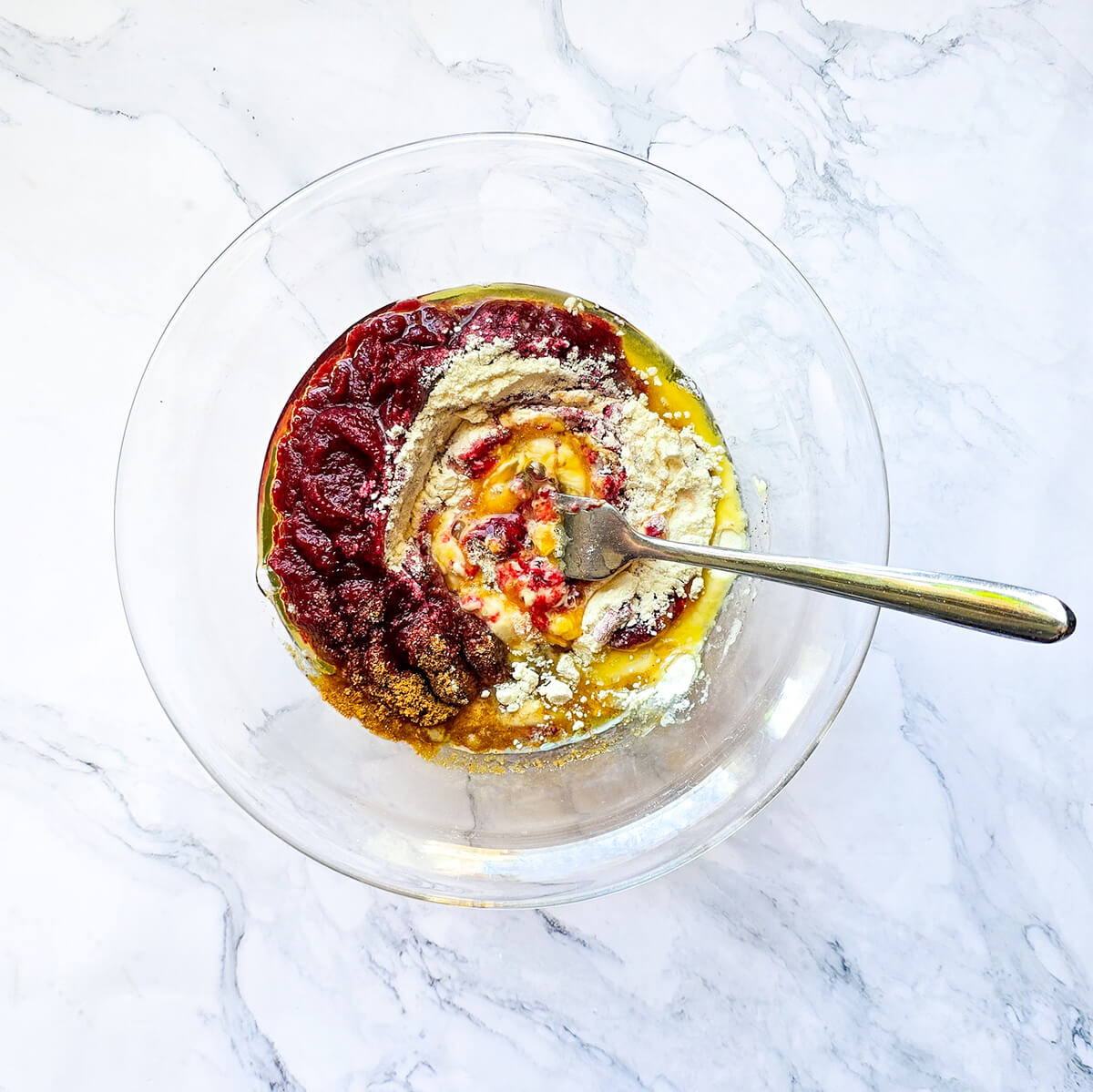 Un mélange d'ingrédients pour wraps dans un saladier transparent, sur fond blanc marbré.