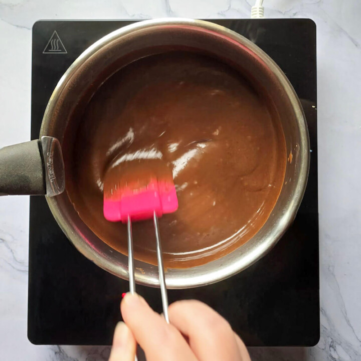 Action de mélanger à la maryse une crème au chocolat lisse et brillante en cours de cuisson dans une casserole sur une plaque à induction.
