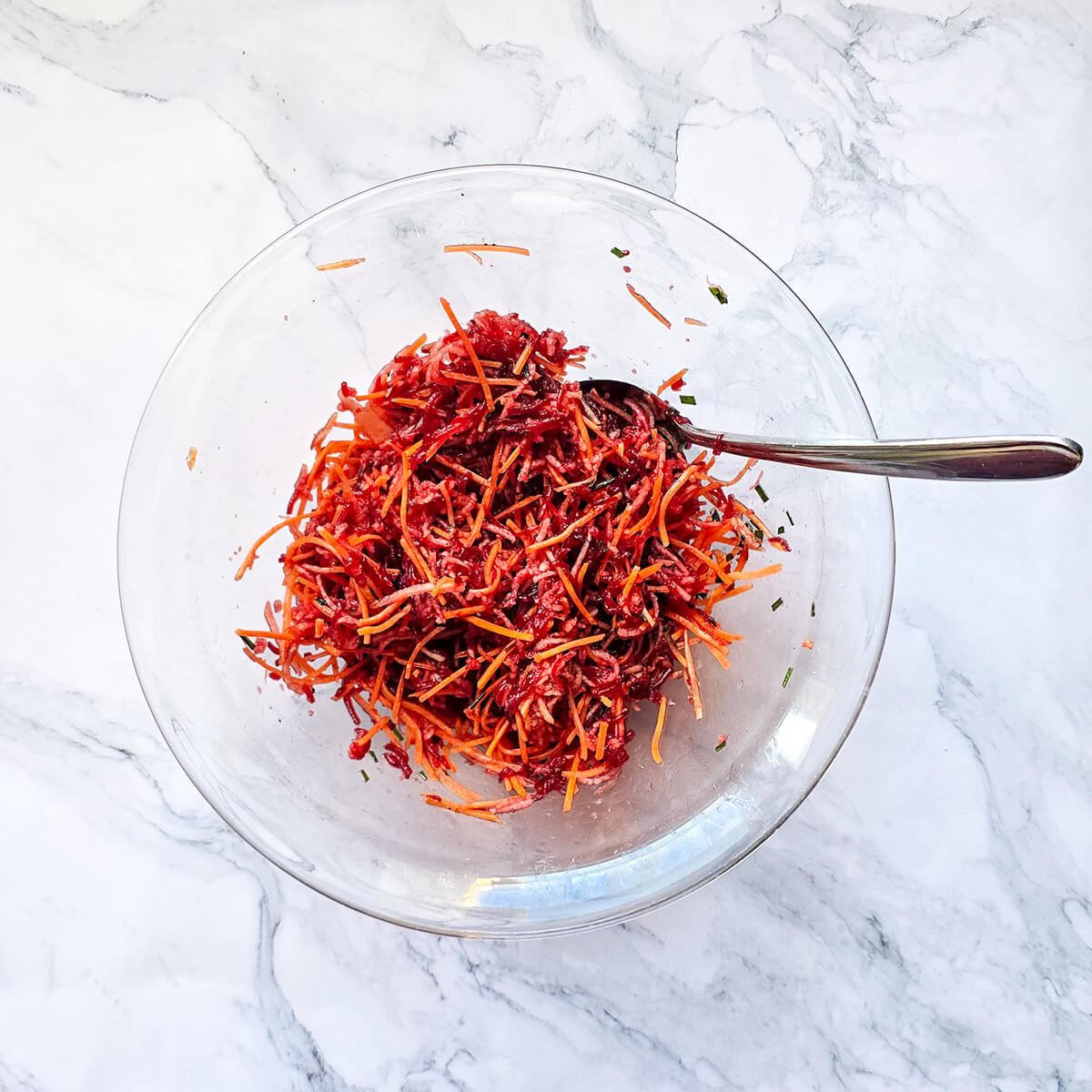 Une salade de betterave dans un saladier transparent, sur un fond marbré blanc.