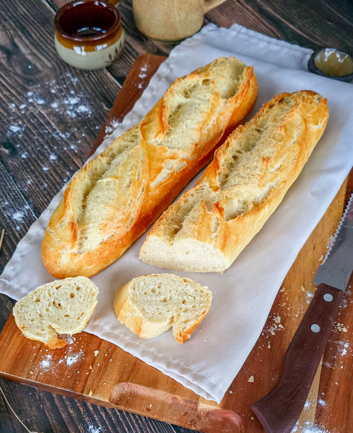Gros plan sur une baguette maison coupée en tranches, révélant une mie aérée et alvéolée, posée sur une planche en bois avec un couteau à pain.
