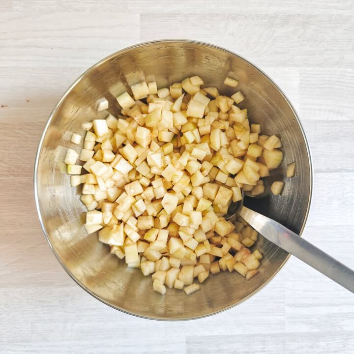 Pommes coupées en petits dés réguliers dans un bol en inox, saupoudrées de cannelle pour une base de crumble aux pommes sans sucre ajouté.