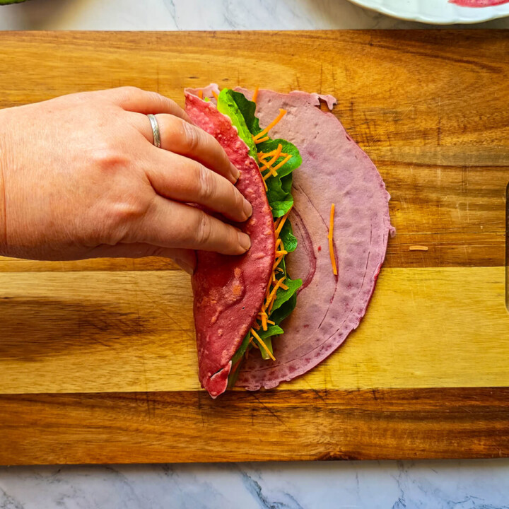 Une main roulant un wrap sur une planche de bois.