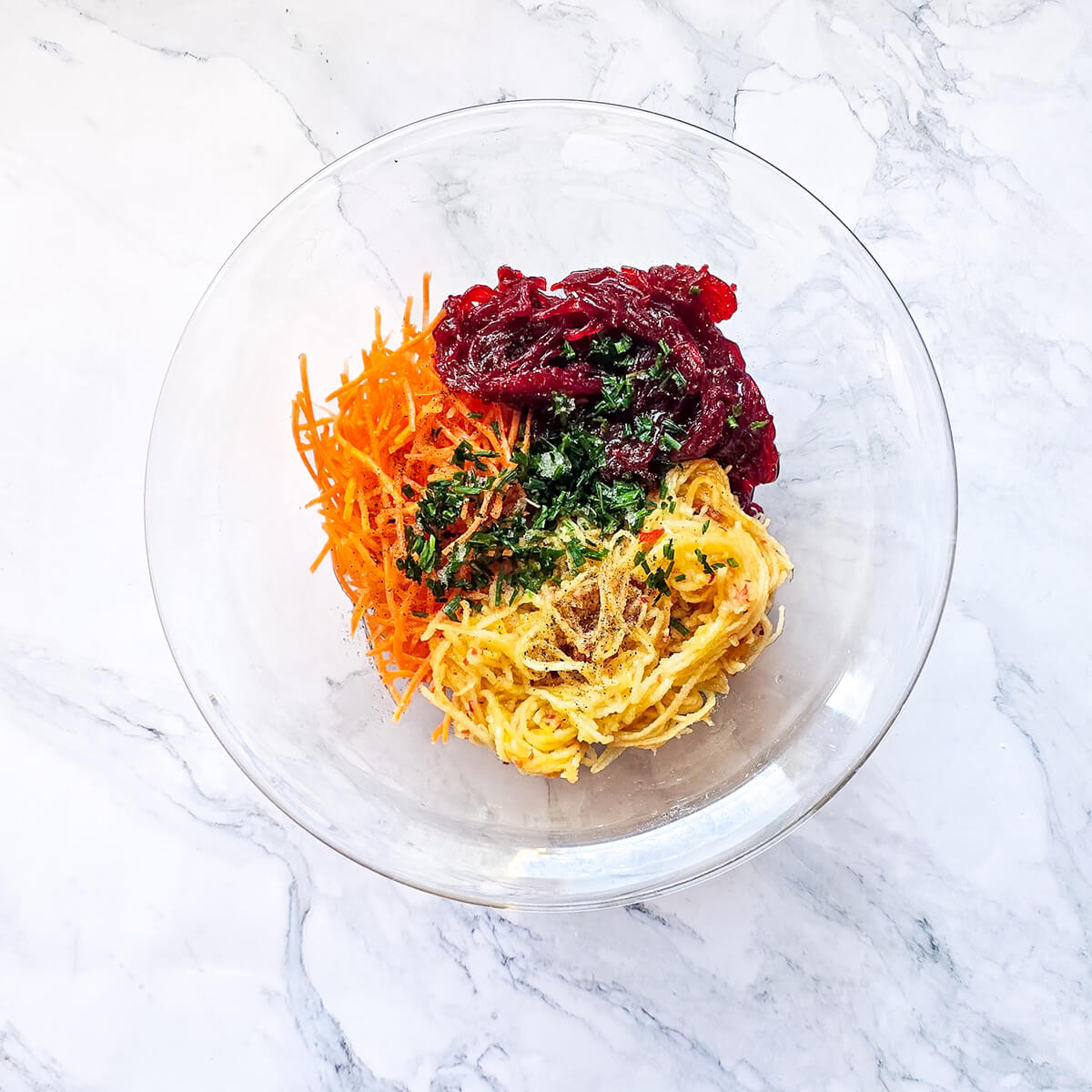 Un mélange de légumes et assaisonnment pour une salade, dans un saladier transparent, sur un fond marbré blanc.