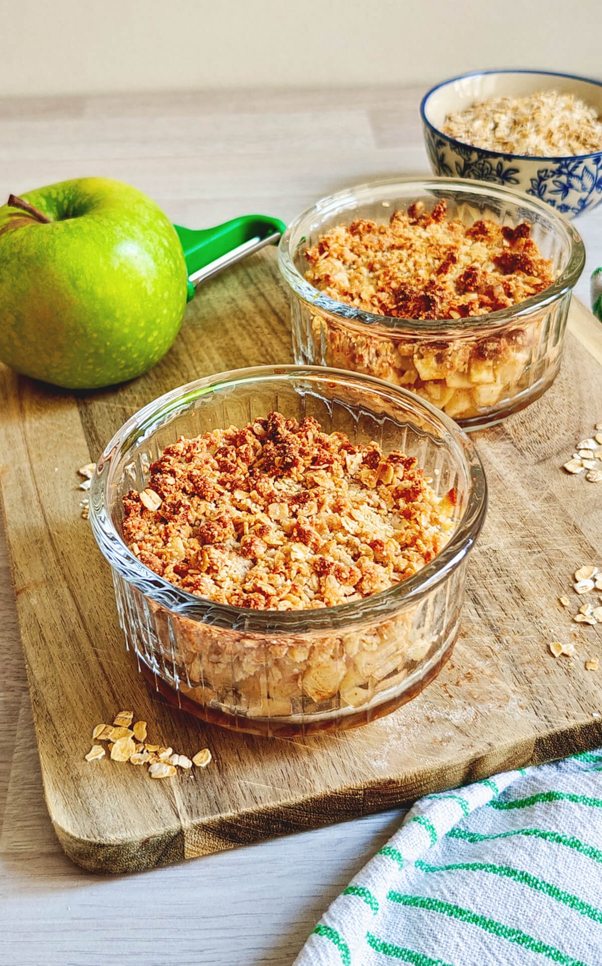Deux ramequins transparents remplis de crumble pomme healthy sur une planche de bois, pomme verte en arrière.