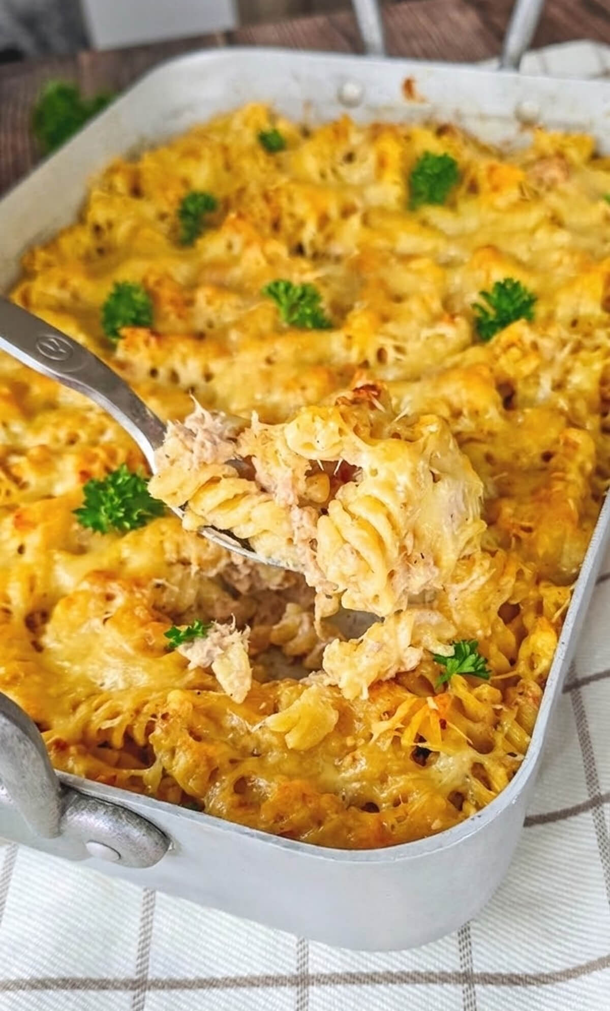 Vue rapprochée d'une part de gratin de pâtes au thon servie à la cuillère, montrant une croûte de fromage bien dorée, une texture onctueuse et quelques feuilles de persil frais en décoration.