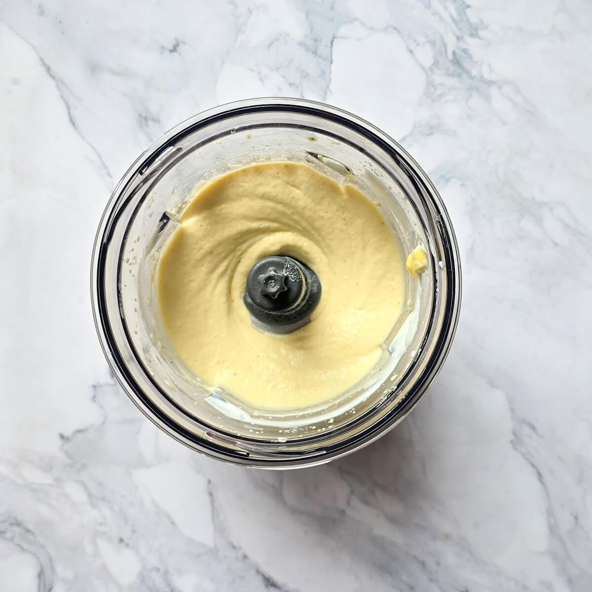 Texture finale de la mayonnaise aux œufs durs et au Skyr après mixage, présentant une consistance lisse, crémeuse et de couleur jaune pâle dans le bol du robot.