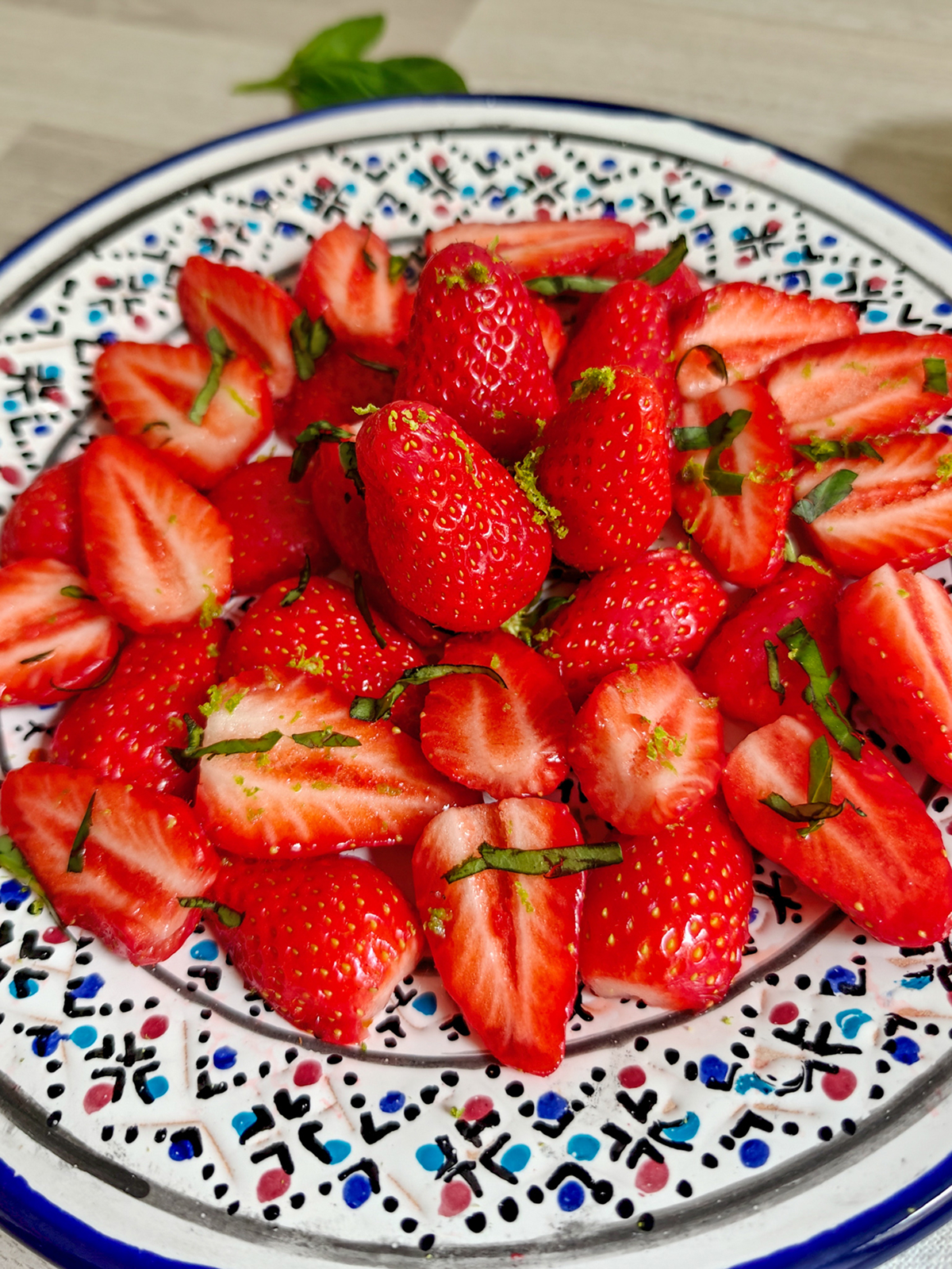 Gros plan sur une salade de fraises fraîches parsemées de basilic ciselé et de zestes de citron vert, présentée dans une assiette artisanale colorée. Un dessert léger, sain et healthy, parfait pour une recette d'été rafraîchissante.