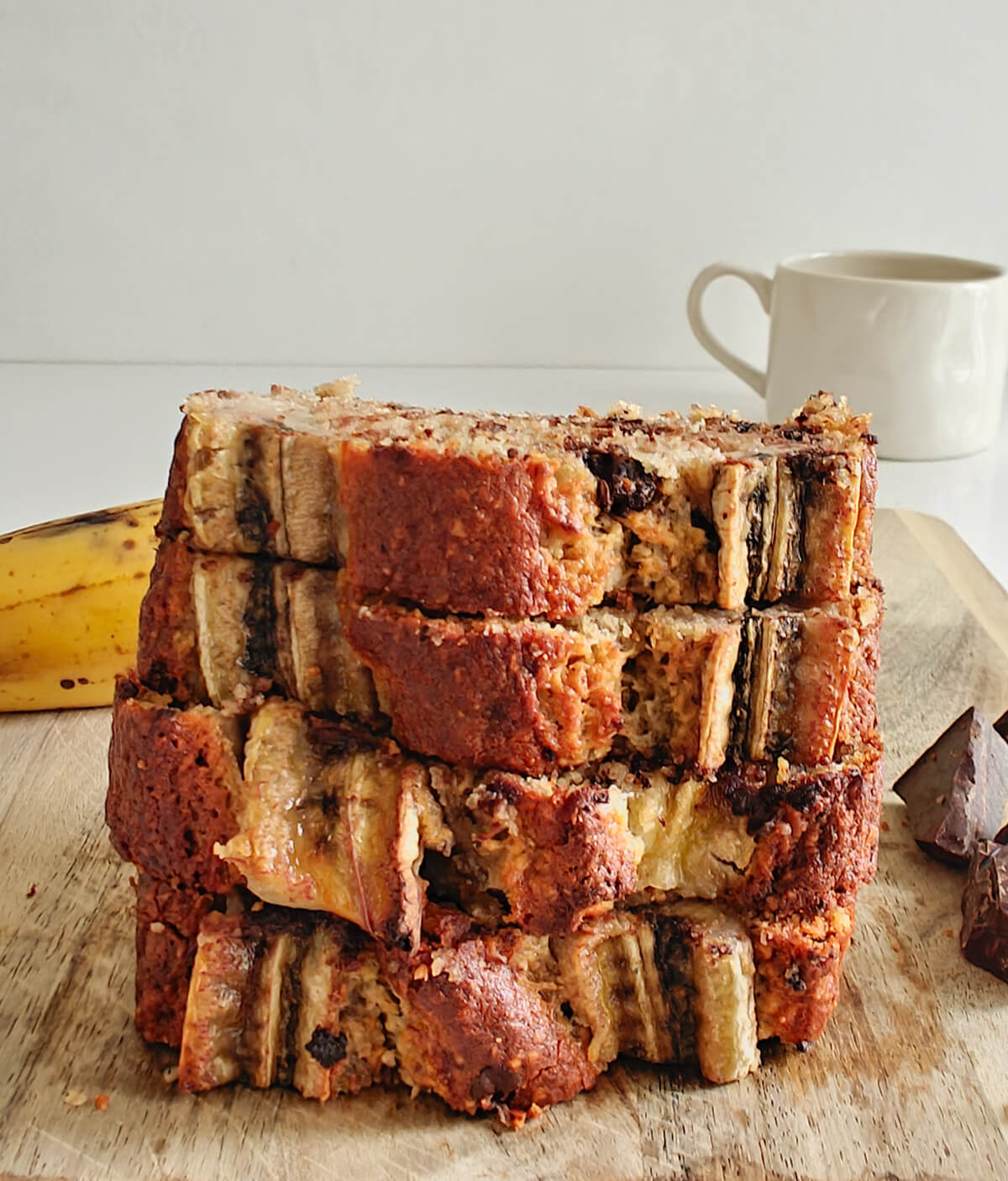 4 grosses tranches de bananes bread empilées les unes sur les autres, sur une planche de bois.