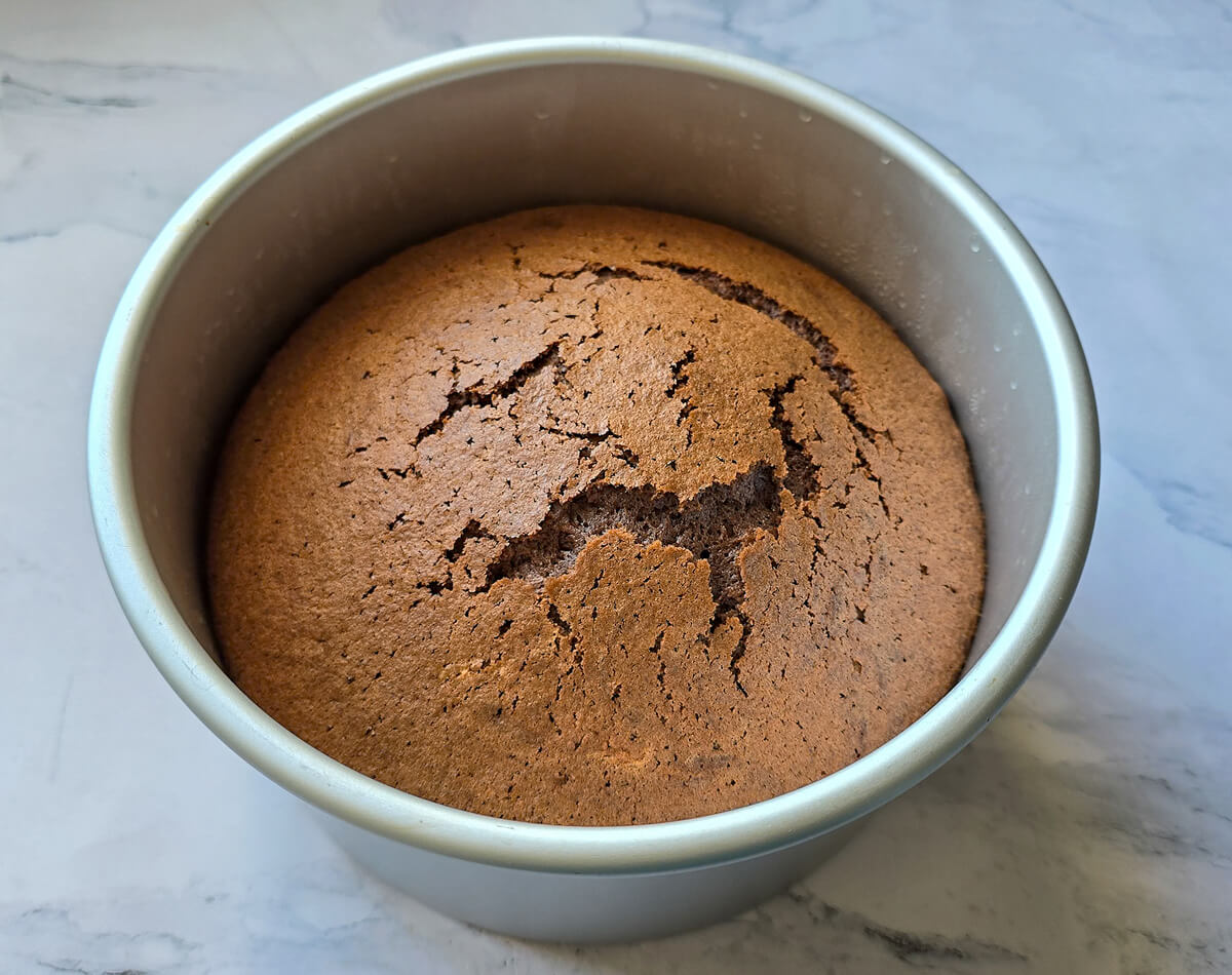 un chiffon cake au cacao cuit, dans son moule rond gris clair, sur une surface blanche marbrée.