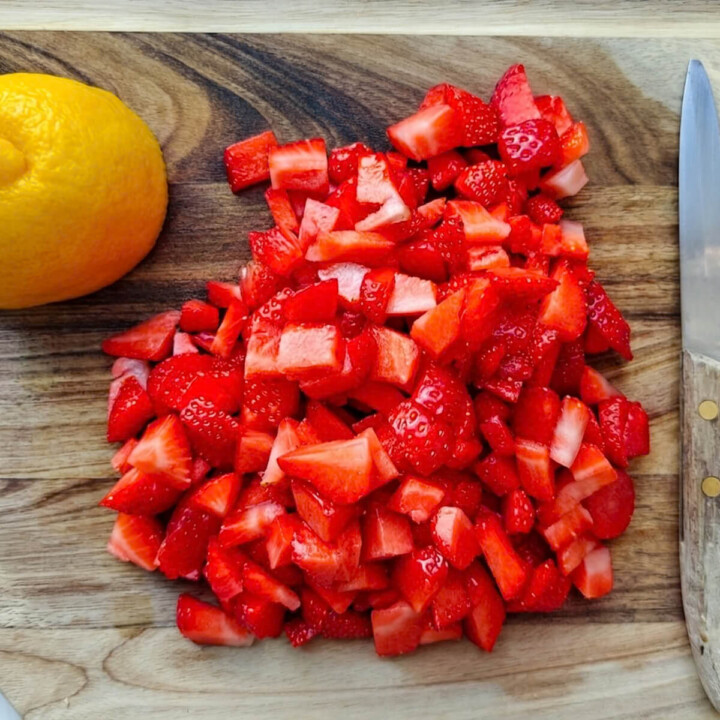 Des fraises fraîches coupées en dés sur une planche en bois à côté d'un citron entier et d'un couteau.