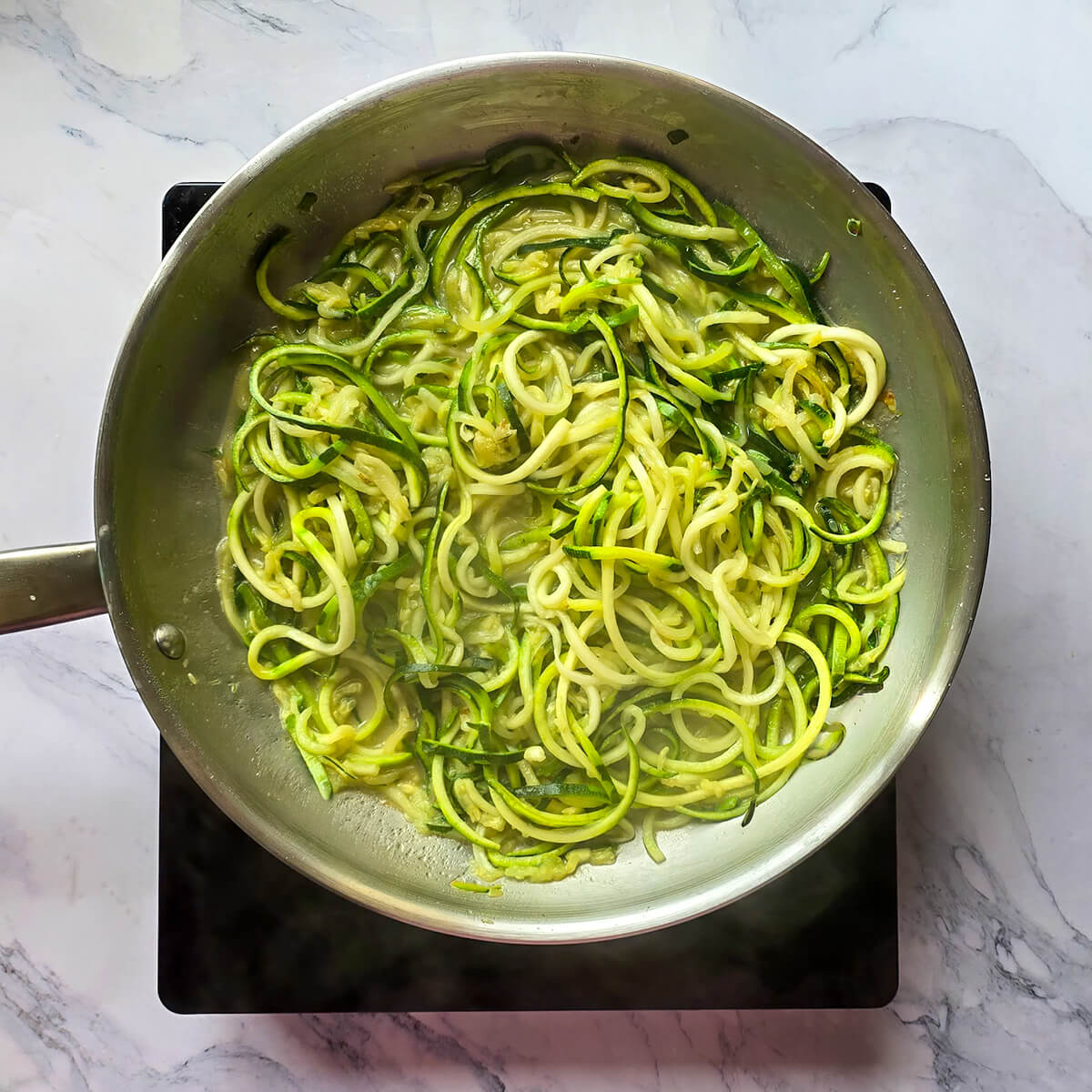 Spaghettis de courgettes fraîches (zoodles) légèrement sautés dans une poêle pour une alternative saine aux pâtes.
