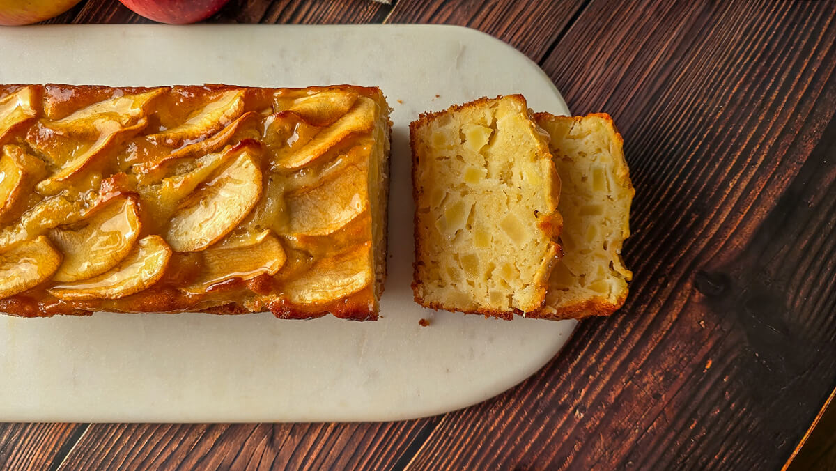 Gros plan d'un gâteau aux pommes fondant décoré de fines lamelles de pommes caramélisées et brillantes, vue de dessus sur une table en bois.