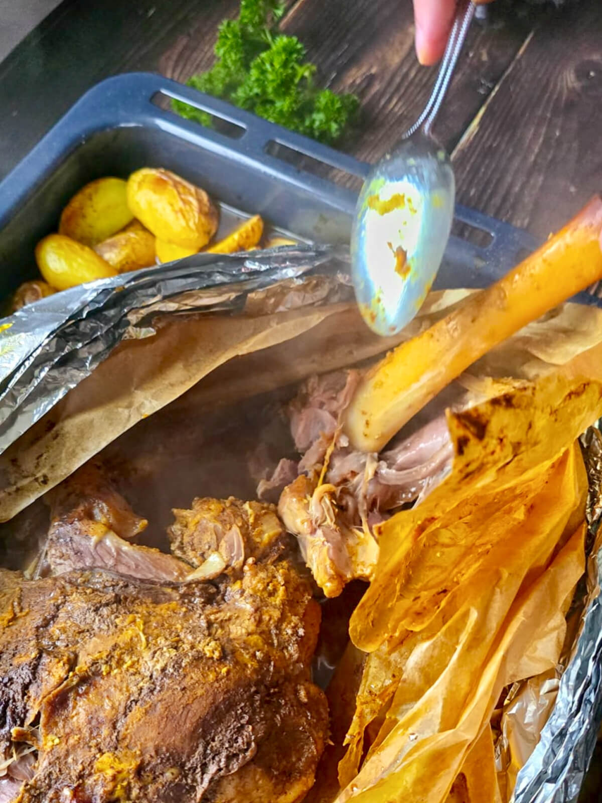 Gros plan sur un gigot d'agneau ultra fondant dont la viande se détache facilement de l'os à l'aide d'une cuillère, révélant une texture effilochée et juteuse après une cuisson en papillote.