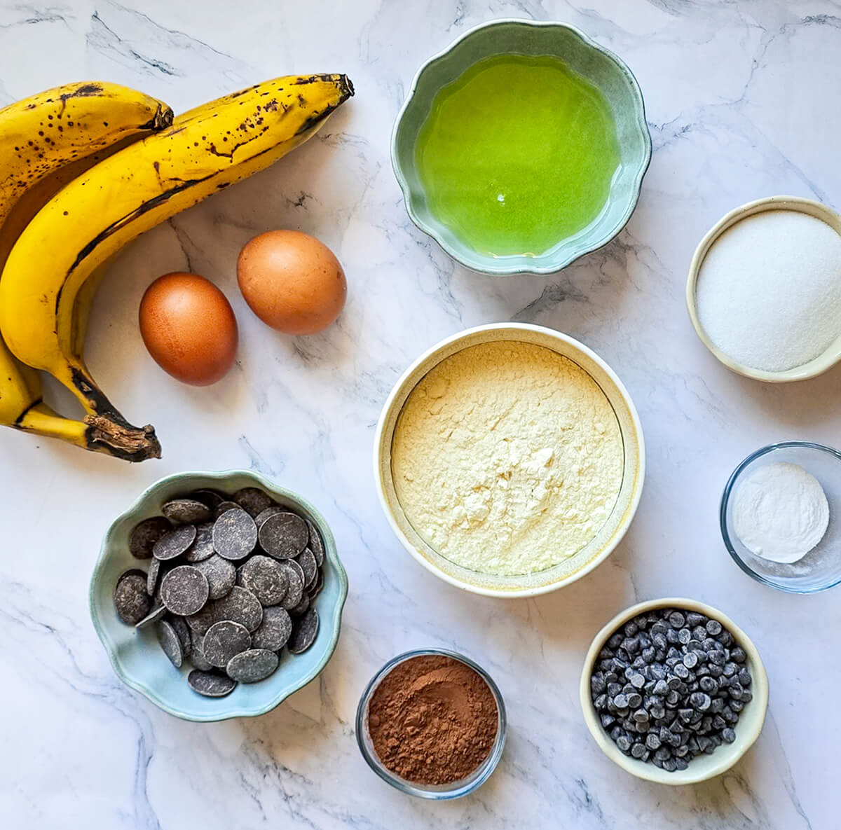 Des ingrédients pour réaliser une recette de banana bread sur un fond blanc marbré.