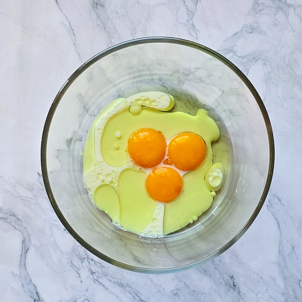 Gros plan sur trois jaunes d'œufs vifs mélangés avec de l'huile et un peu de lait dans un petit bol en verre, formant une base liquide pour la pâte du chiffon cake.