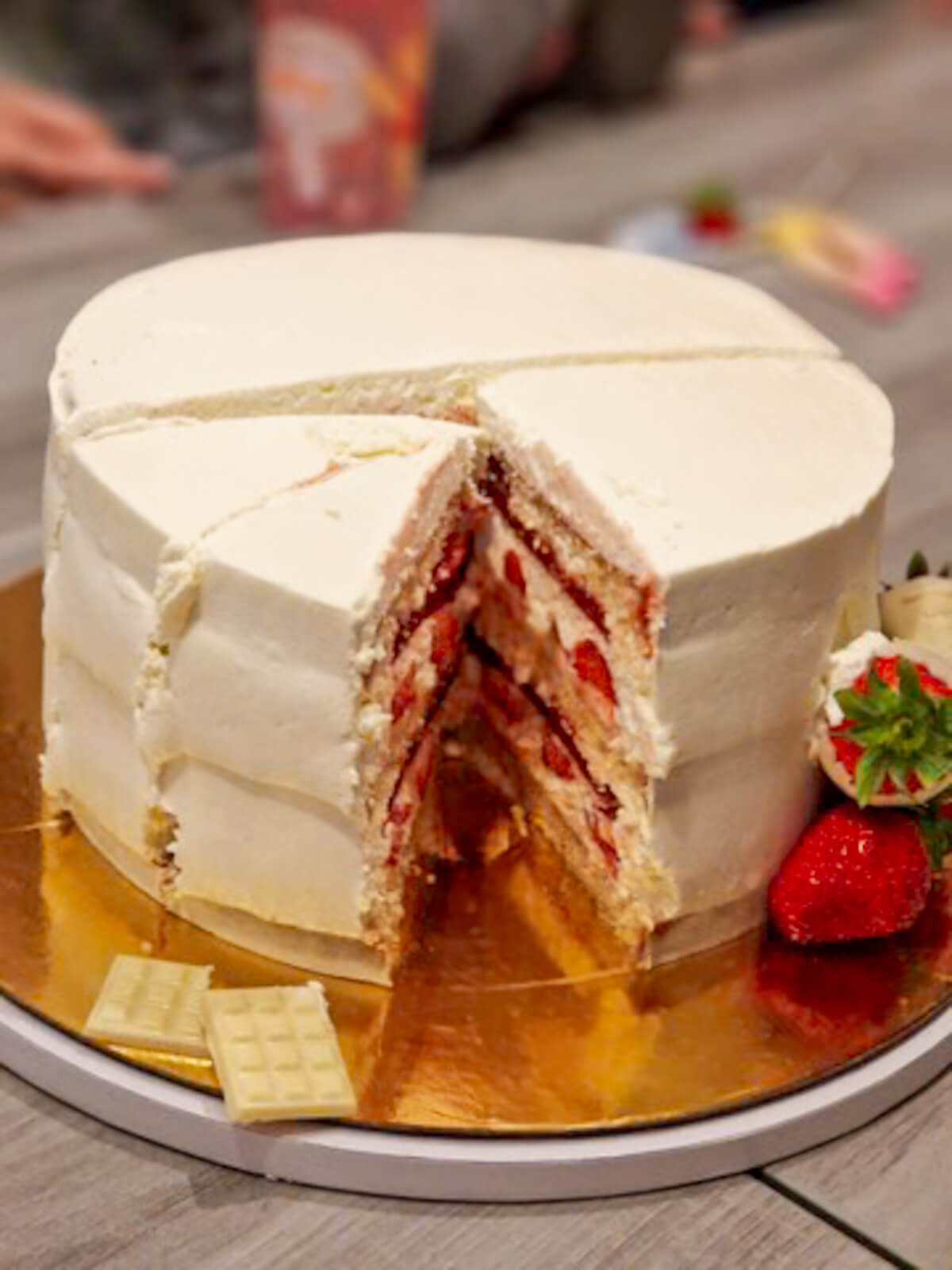 Une part découpée d'un layer cake fraise vanille sur un support doré, révélant les couches de biscuit Molly Cake moelleux, la ganache montée vanille et l'insert gélifié aux fraises fraîches.