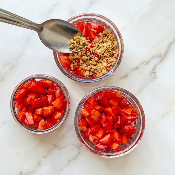 Montage de trois verrines de fraises où l'on dépose du crumble à la cuillère sur les fruits.