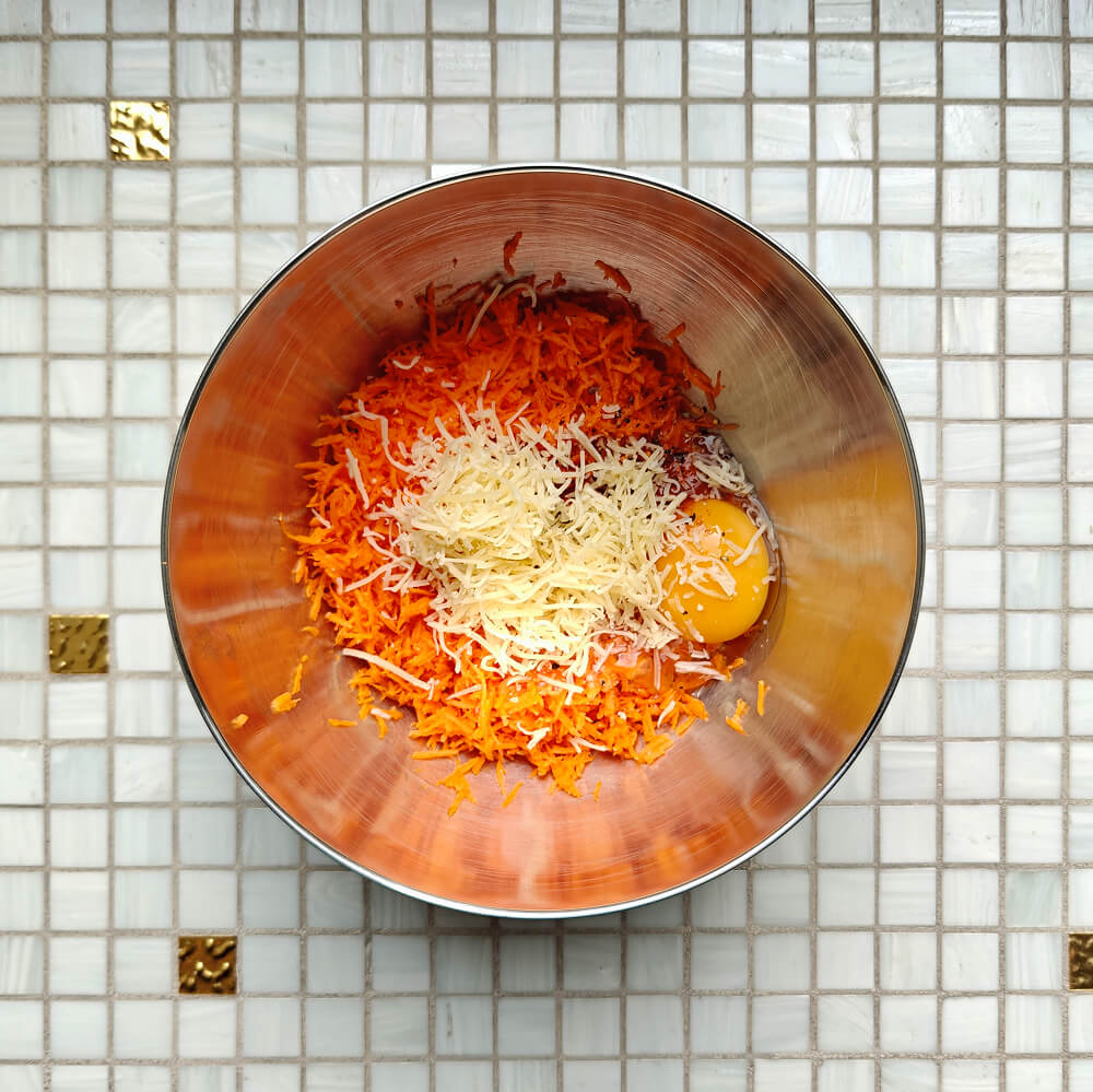 Mélange de carottes râpées, d'œuf et de fromage râpé dans un bol en inox pour préparer la pâte d'un wrap à la carotte maison.