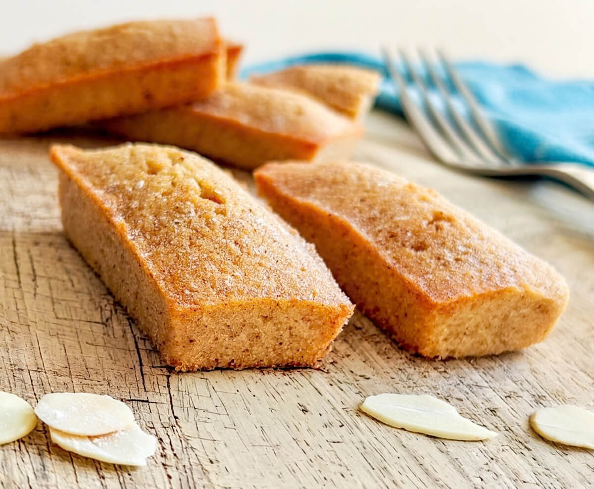 Deux financiers sur une planche de bois, amandes effilées sur le côté.