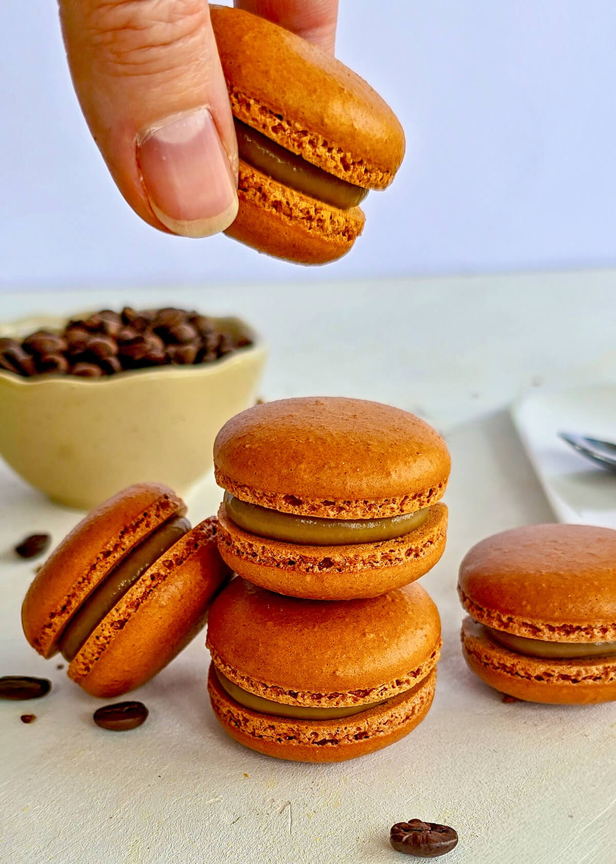 Une main tenant un macaron au café, avec d'autres macarons empilés les uns sur les autres.