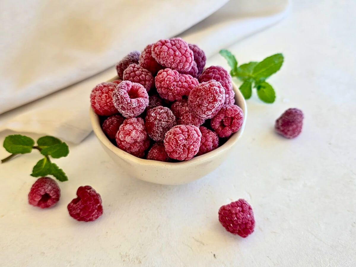 Des framboises surgelées dans un petit bol blanc, menthe fraîche et framboises sur le côté.